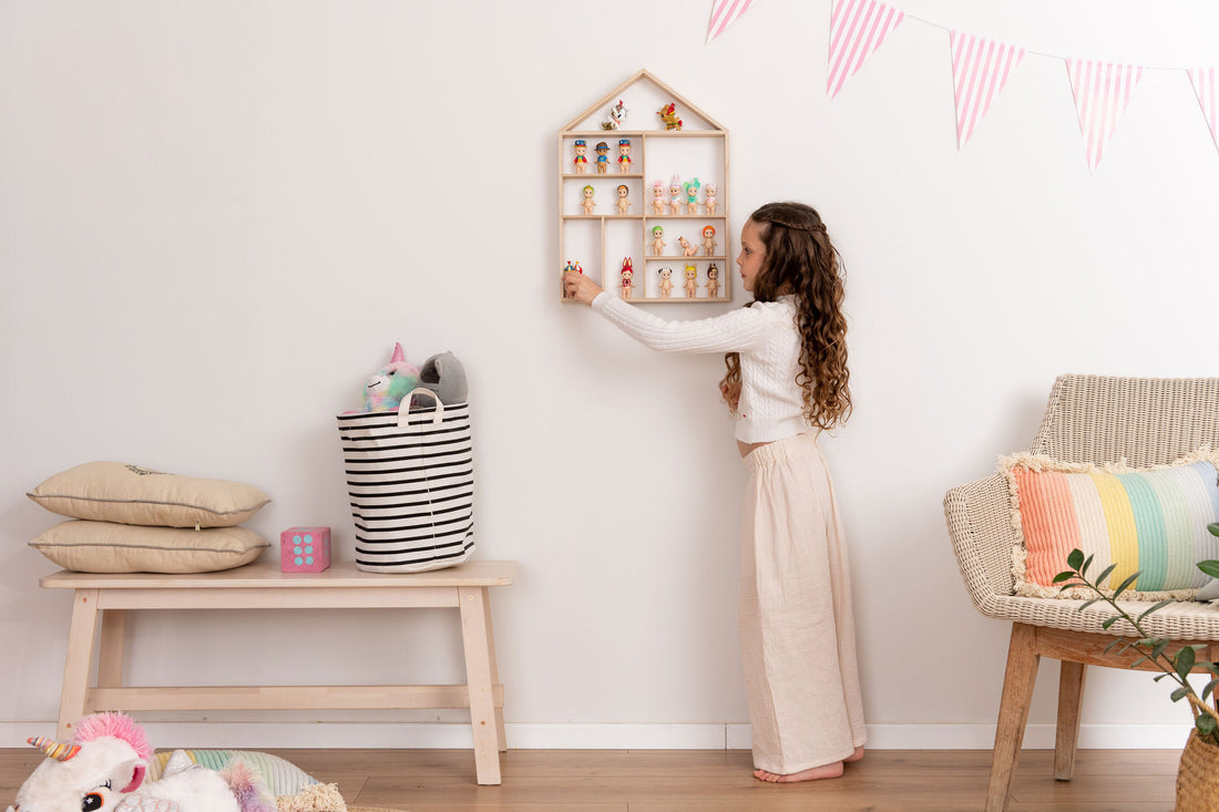 Girl arranging sonny angels dolls on a house-shaped wooden toy display shelf that is hung on the wall