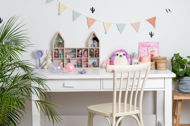 A girl's desk and chair with a castle-shaped wooden toy display shelf standing on it with LOL dolls (with greenery)