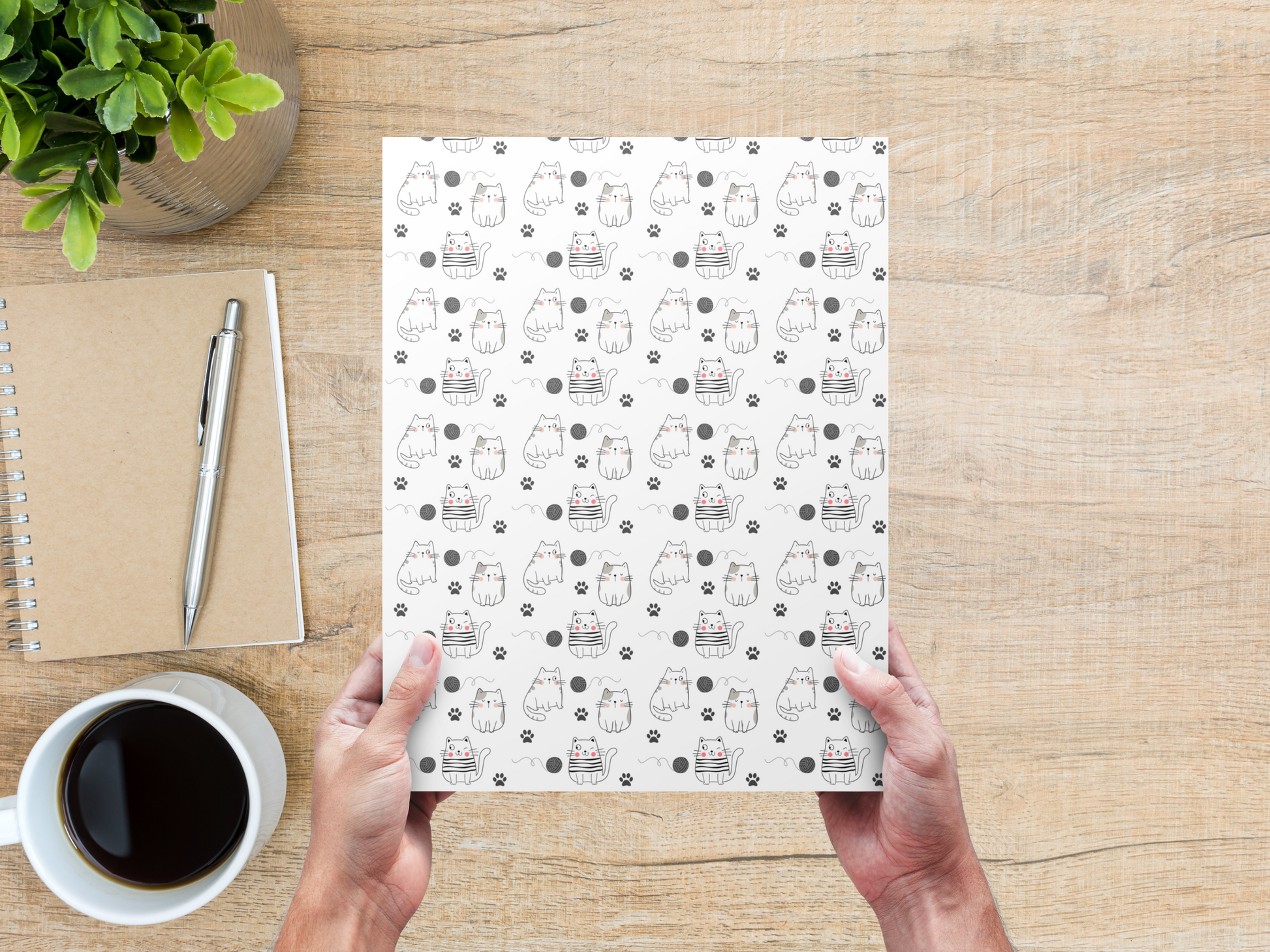 The dollhouse wallpaper pattern of cute kittens is held by a woman above a desk