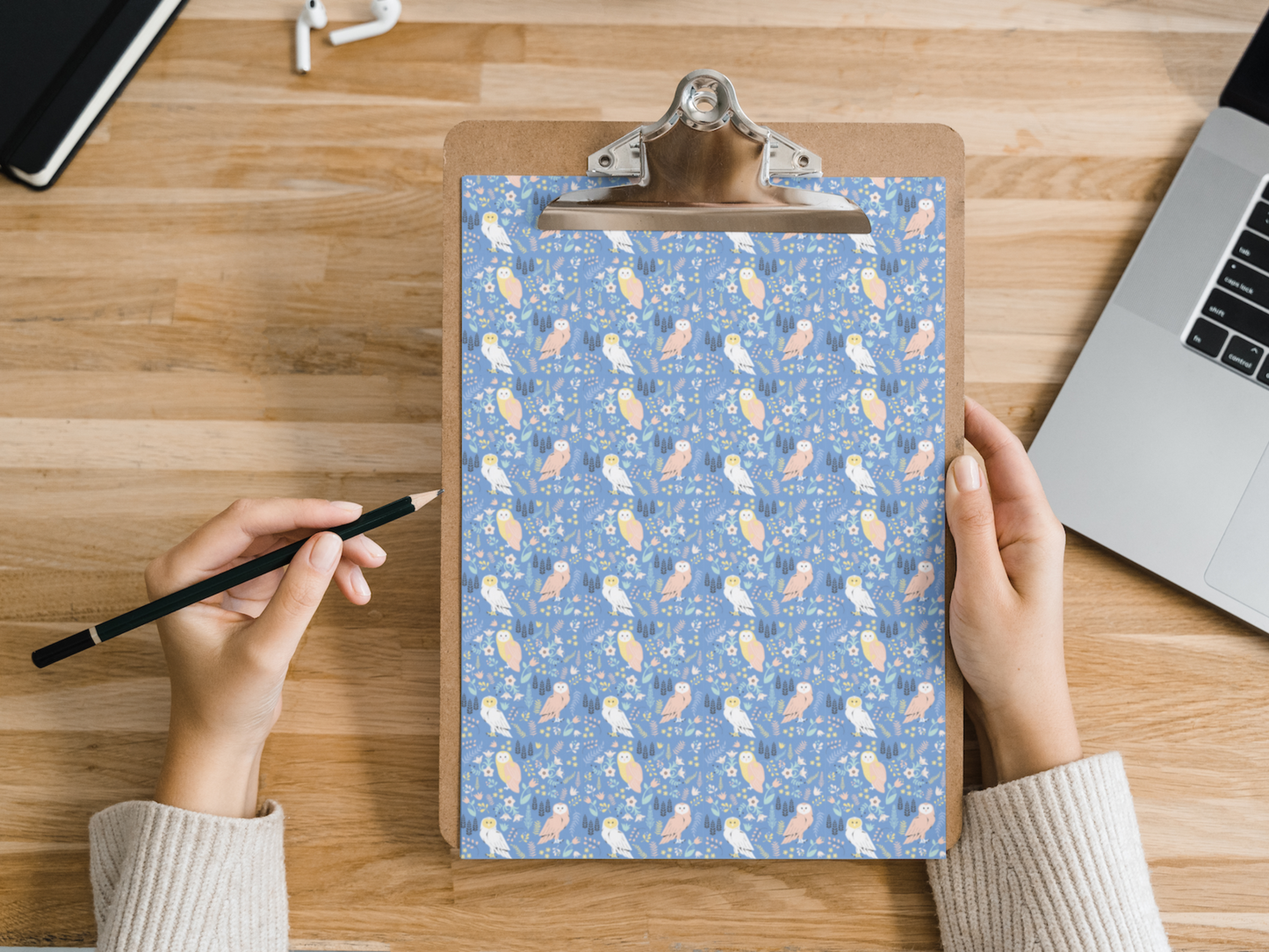 The dollhouse wallpaper pattern of adorable owls is held by a woman above a desk