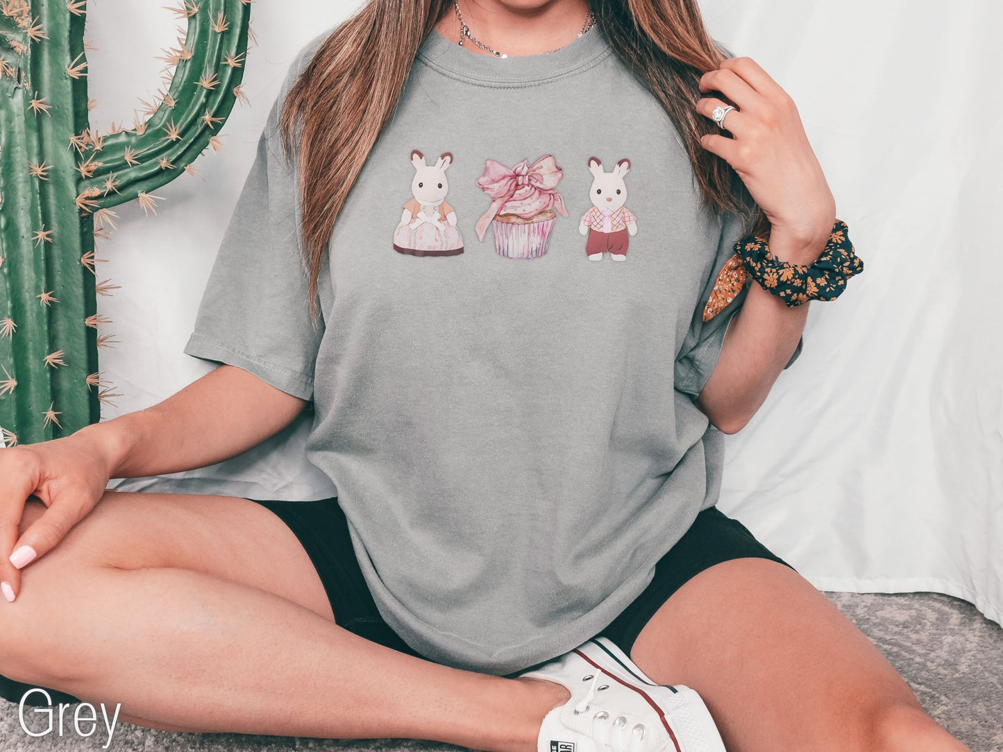 Person wearing a gray t-shirt with cartoon designs sitting on the floor next to a cactus plant.