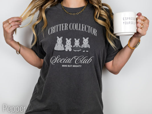 Person wearing a dark gray t-shirt with 'Critter Collector Social Club' text and graphics, holding a mug.