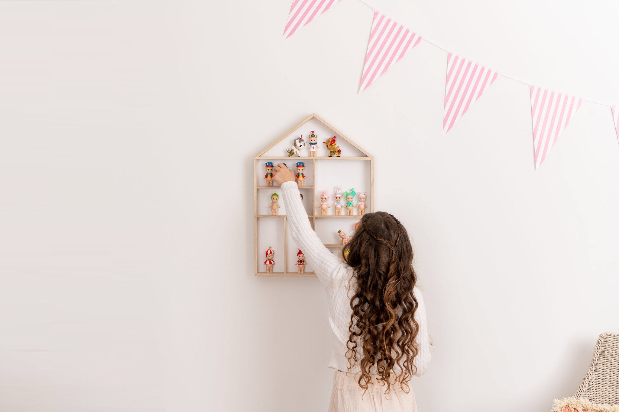 Girl facing the wall playing with Sonny Angels on a house-shaped wooden toy display shelf that is hung on the wall