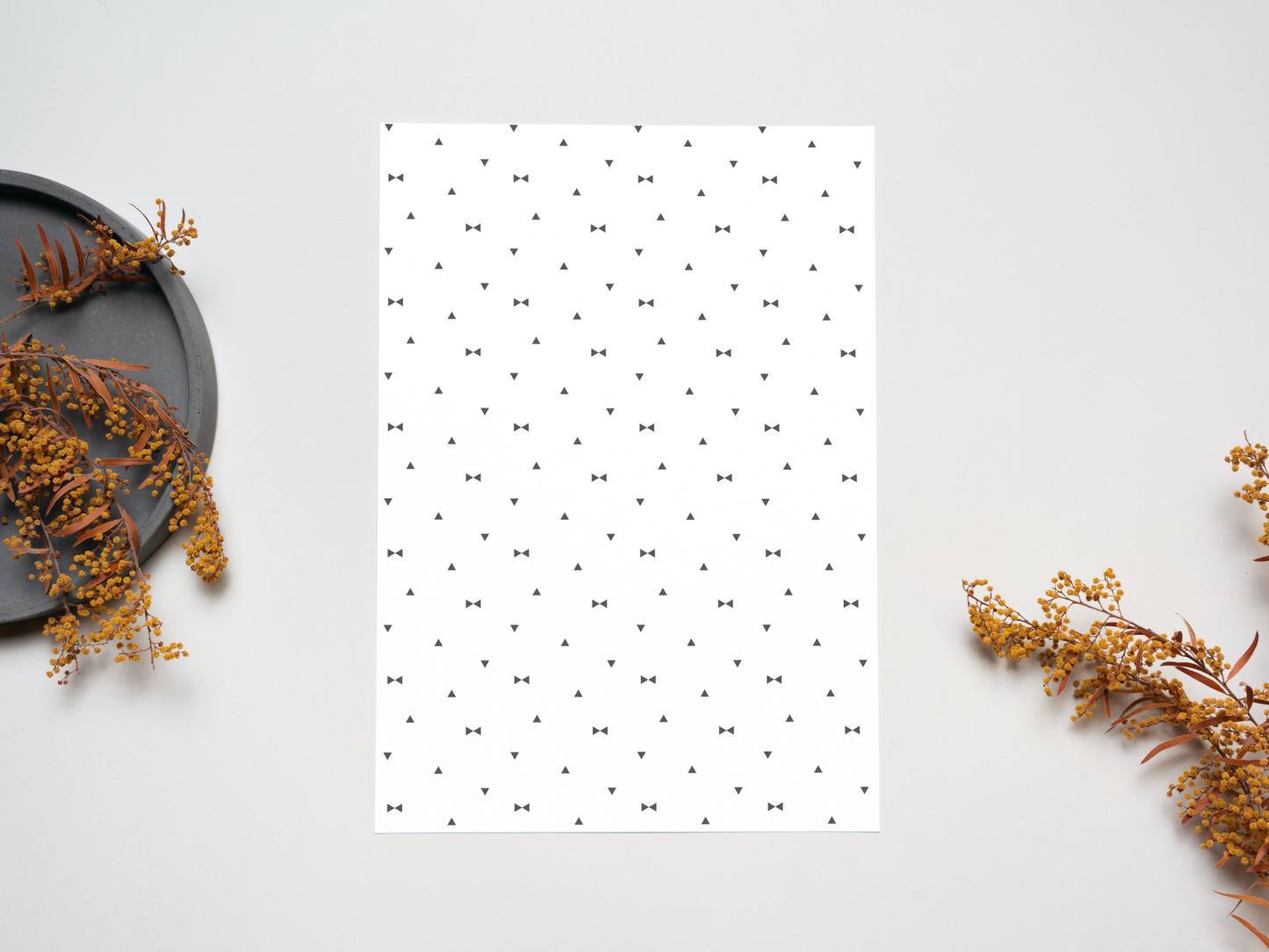 The dollhouse wallpaper pattern of Nordic style little black triangles is set on a table near some dry leaves