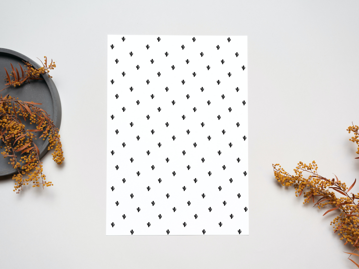 The dollhouse wallpaper pattern of Nordic style little black cacti is set on a table near some dry leaves