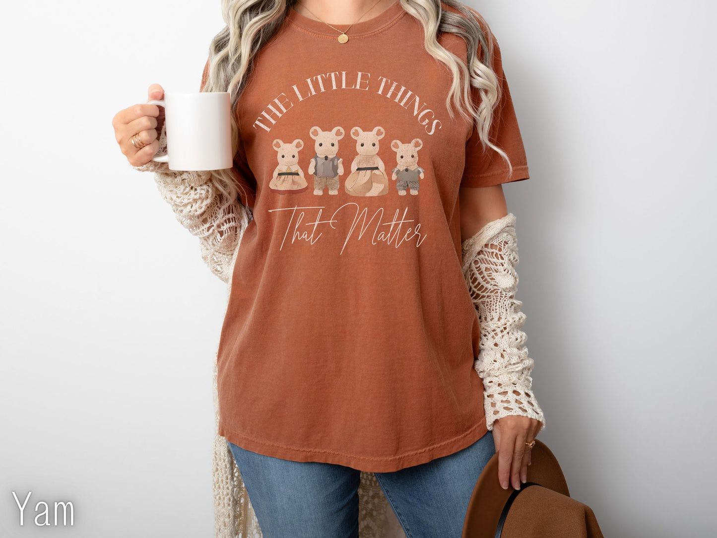 Person wearing a brown t-shirt with a graphic design and holding a mug.