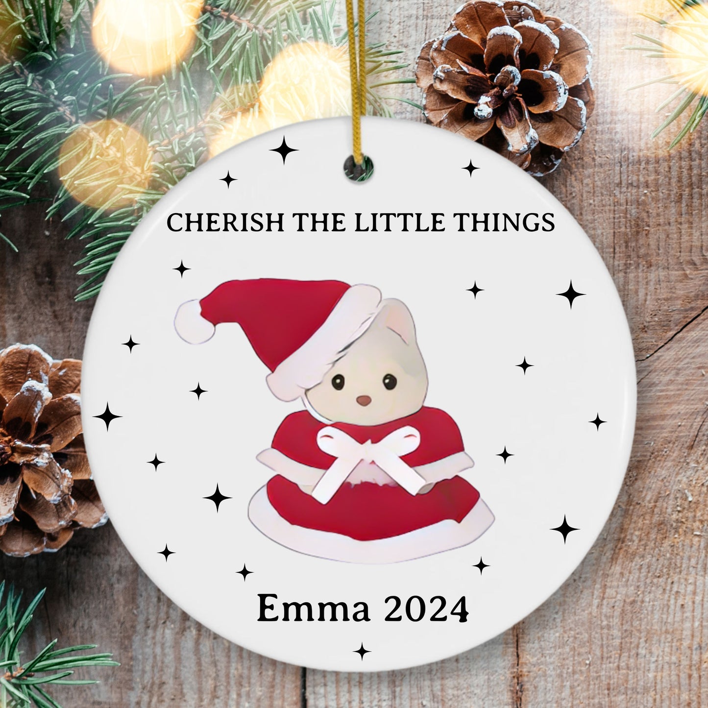 Christmas ornament with a calico critter bear in a Santa hat and text 'Cherish the Little Things' on a wooden background.