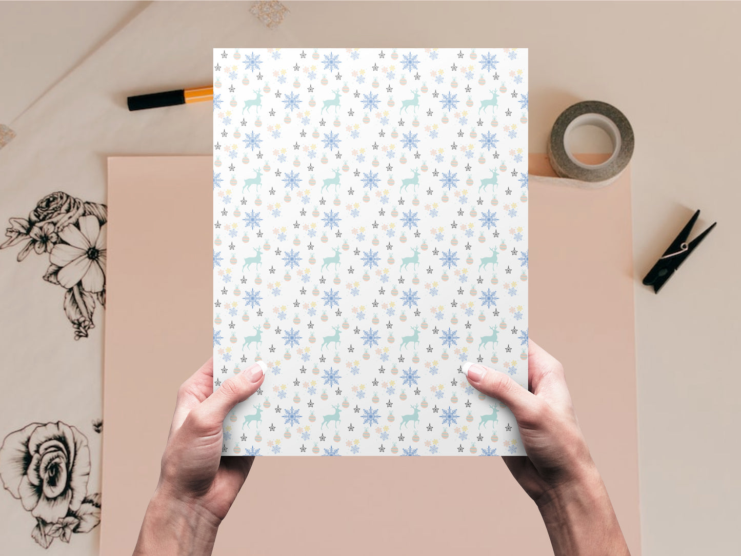 The dollhouse wallpaper pattern of snowflakes, Christmas ornaments, and deer is held by a woman above a desk