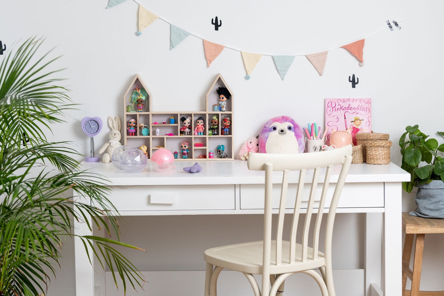 A girl's desk and chair with a castle-shaped wooden toy display shelf standing on it with LOL dolls (with greenery)
