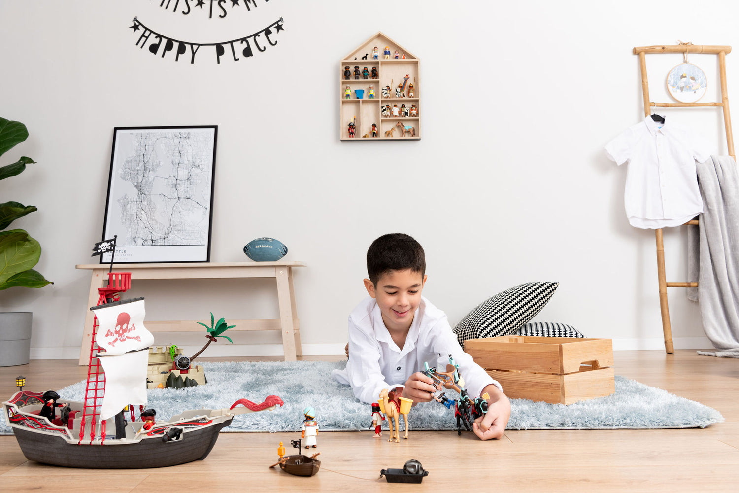 Boy playing with Playmobil near a house shaped wooden shelf with black painted outer walls that is hanged on the wall