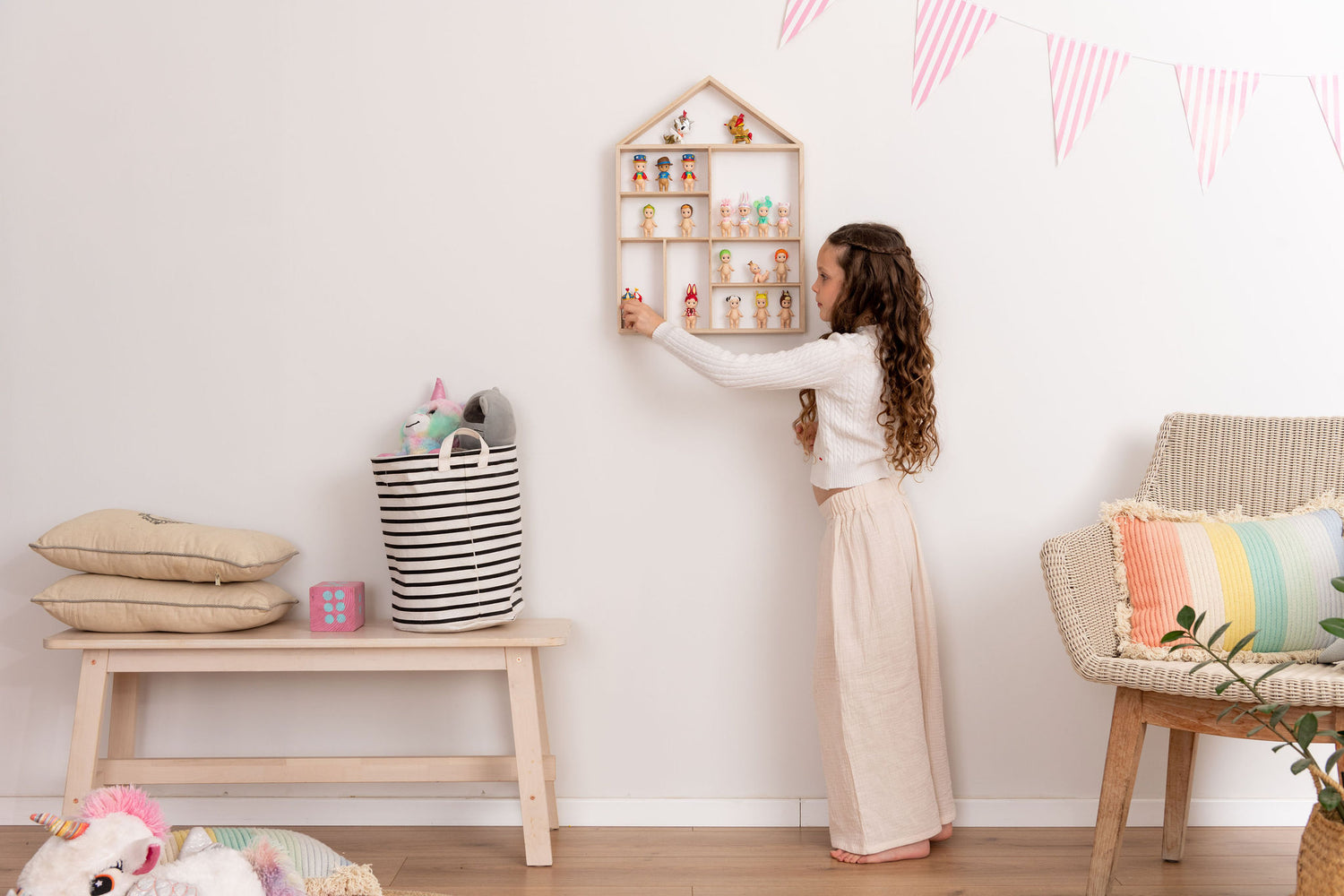 Girl placing a sonny angel doll in a house-shaped wooden toy display shelf that is hung on the wall