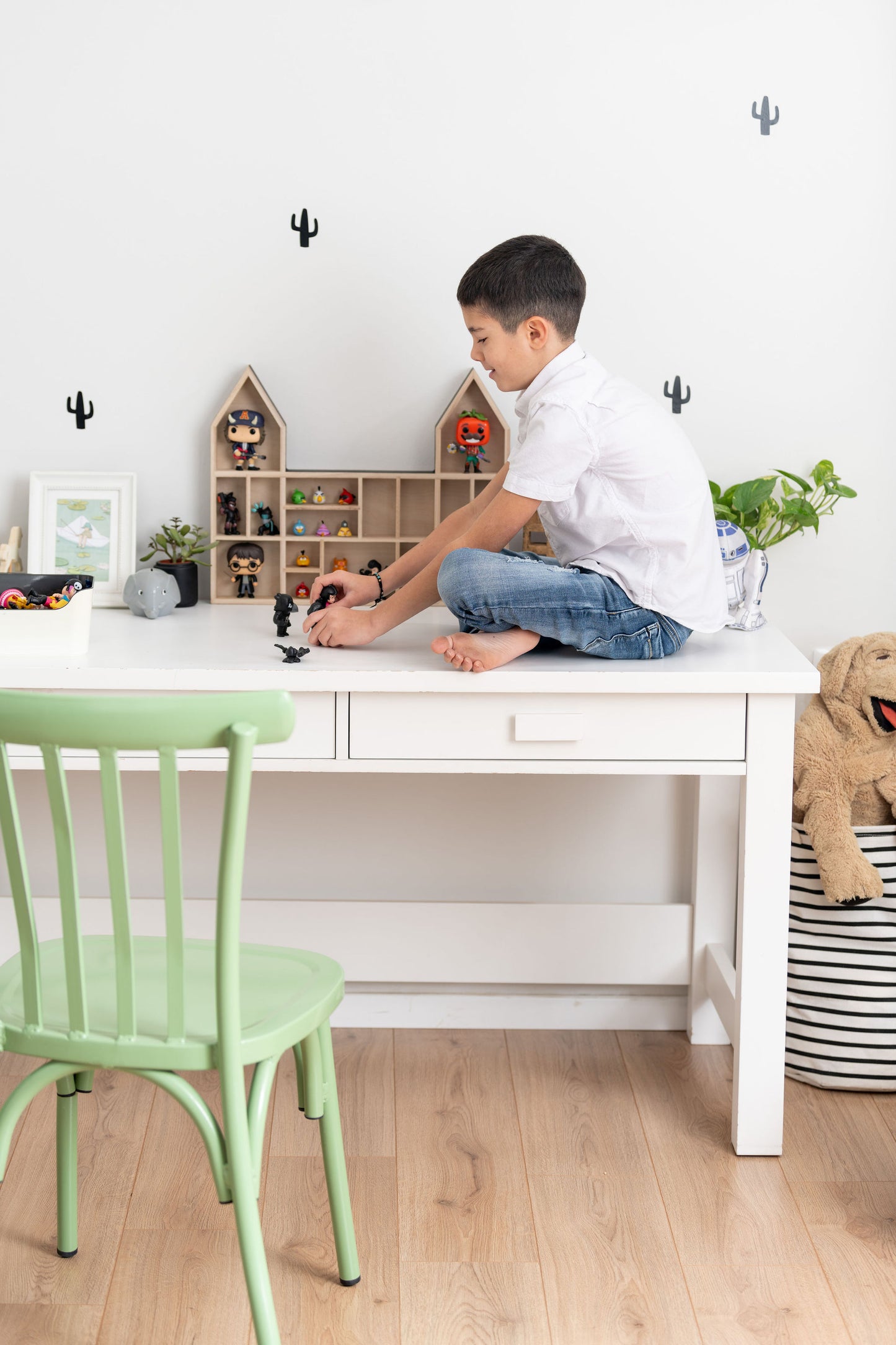 Boy sitting on a desk playing with mini-figures near a castle-shaped wooden toy display shelf