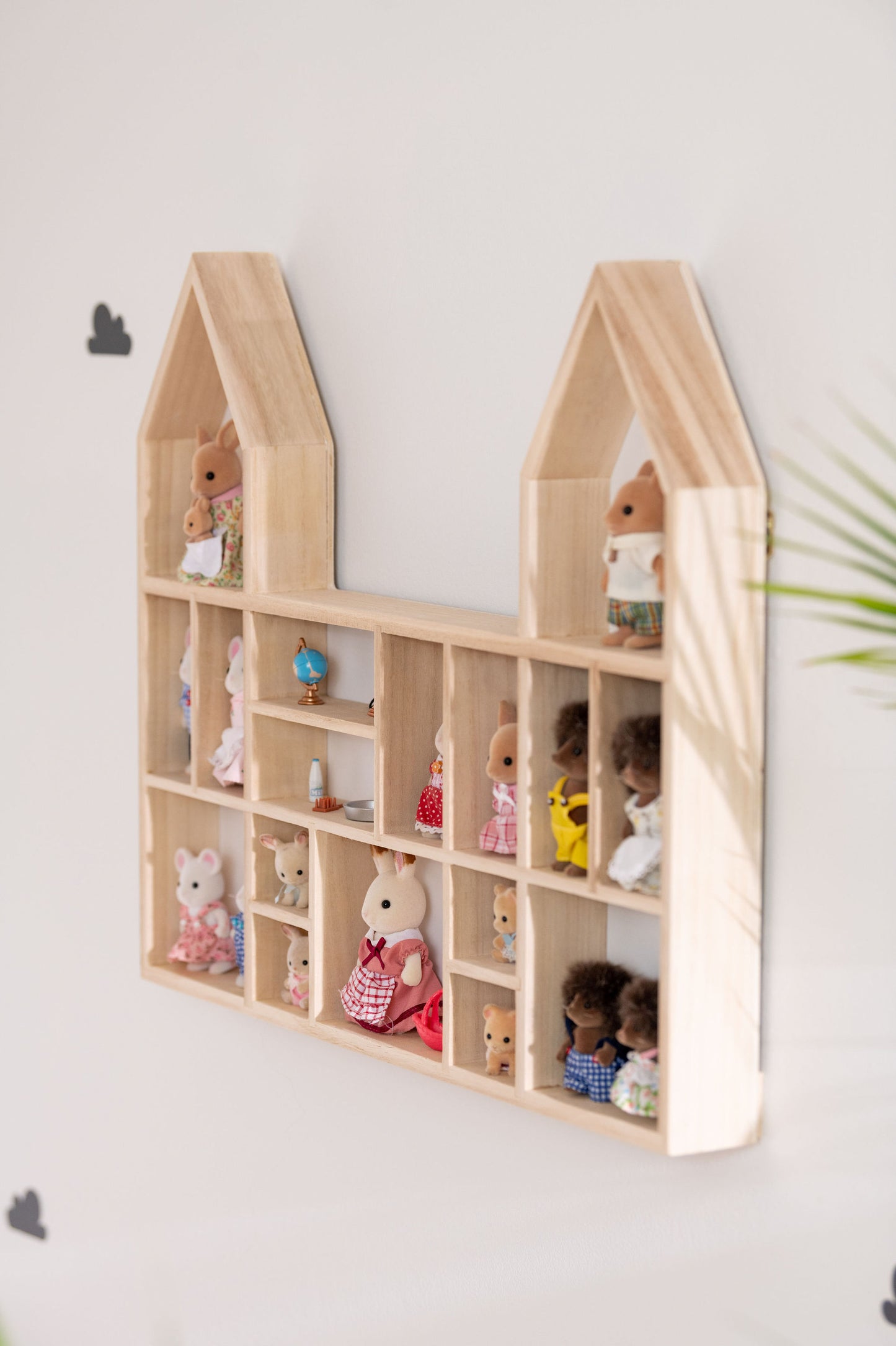 A side view of a castle-shaped wooden toy display shelf with Calico Critters hung on the wall