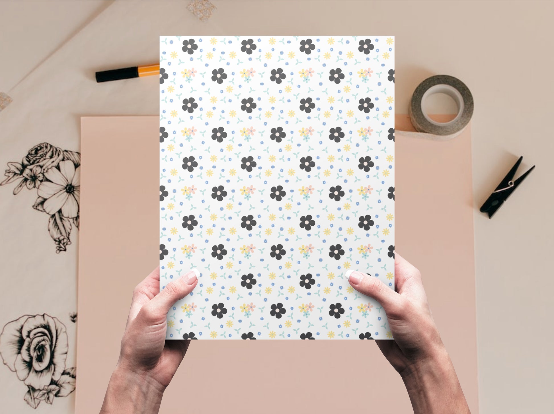 The dollhouse wallpaper pattern of black and pastel flowers is held by a woman above a desk