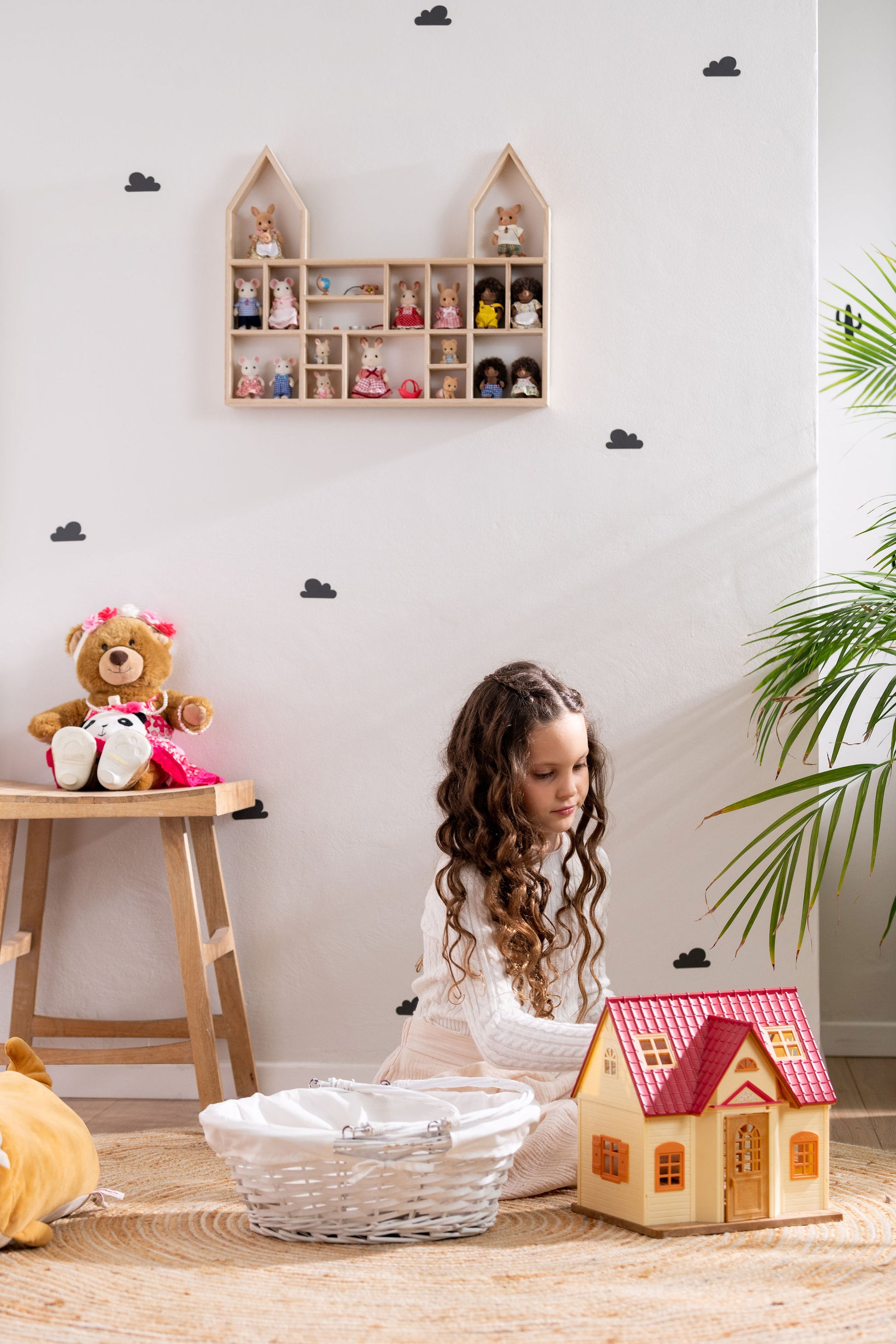 A girl is playing with a Calico Critters house near a castle-shaped display shelf that is hung on the wall