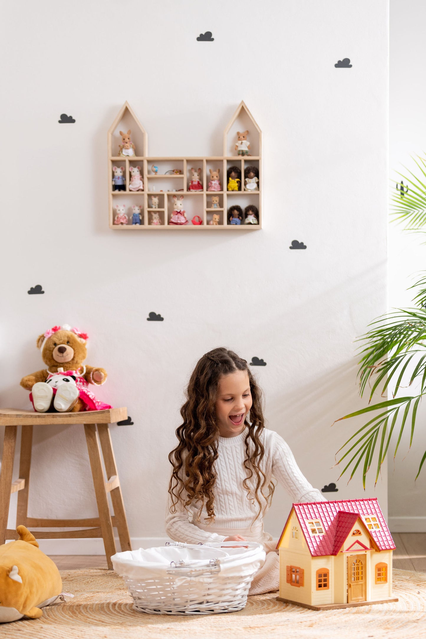 A girl is happily playing with Calico Critters near a castle-shaped wooden toy display shelf that is hung on the wall