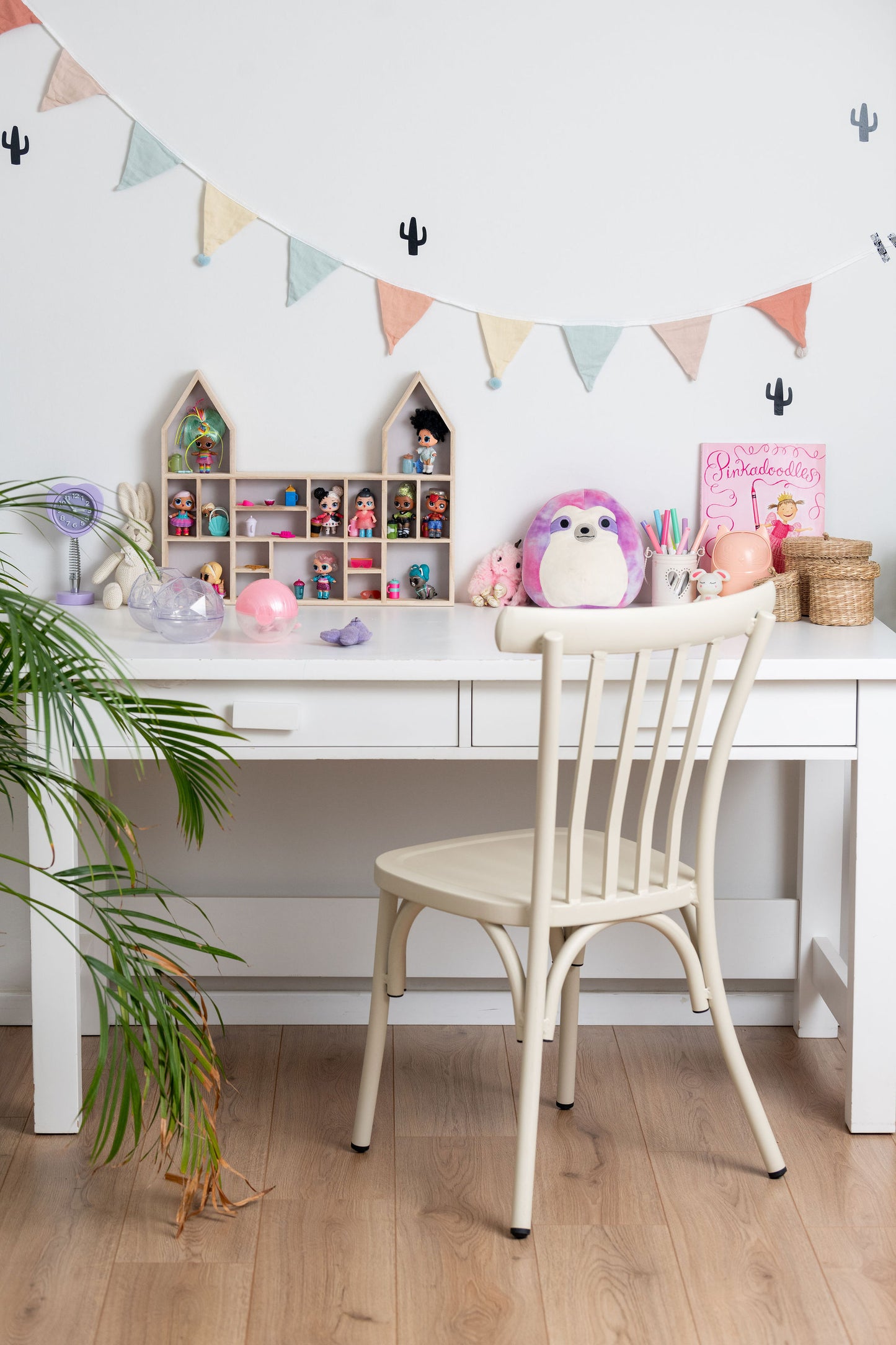 A girl's desk and chair with a castle-shaped wooden toy display shelf standing on it with LOL dolls