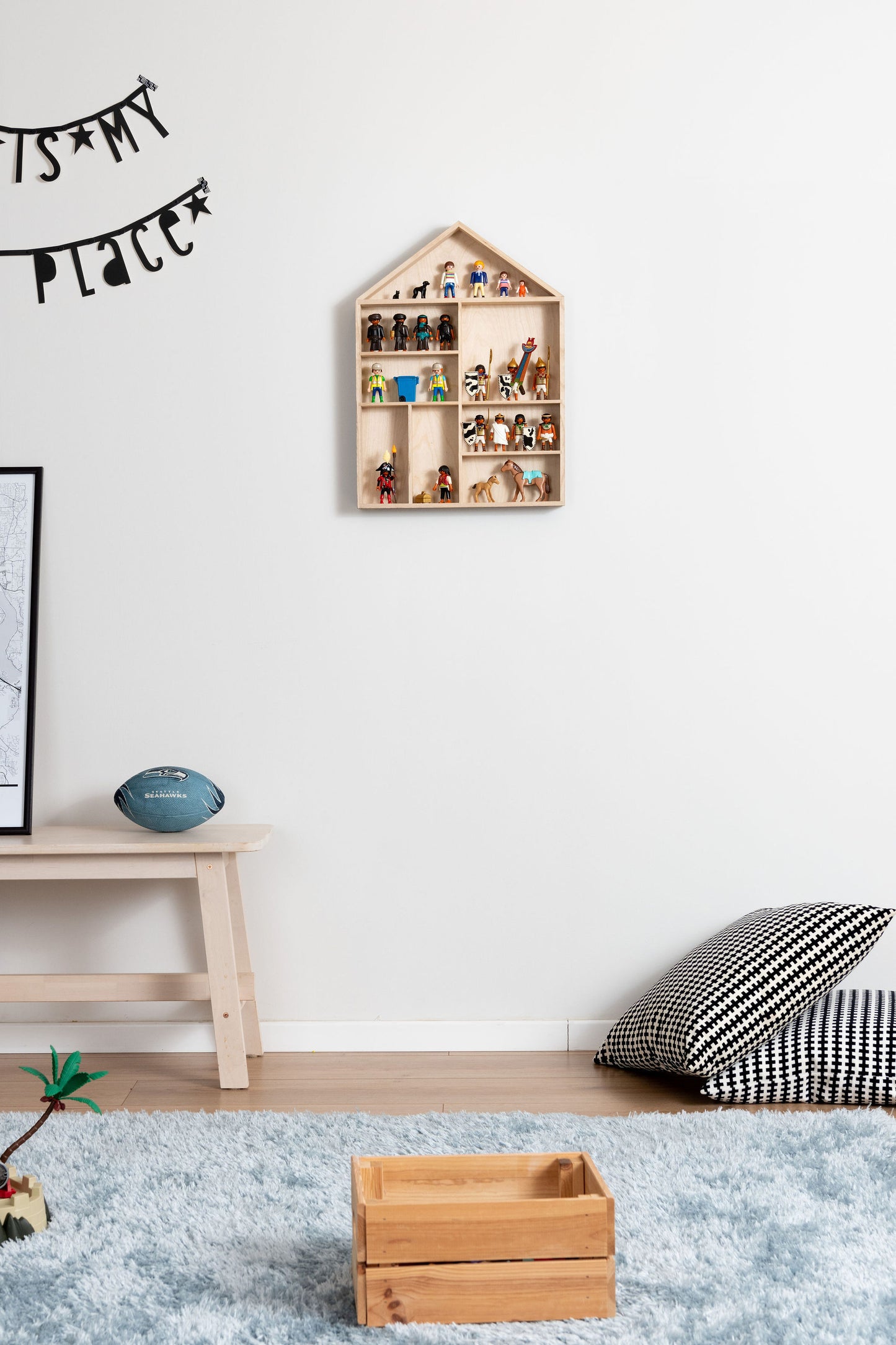 A house-shaped wooden toy display shelf with Playmobil hung on the wall in a boy's room